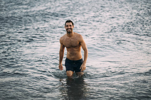 Shirtless lächelnd Mitte erwachsenen Mann waten im Meer bei Sonnenuntergang - MPPF01010