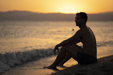Nachdenklicher Mann ohne Hemd, der bei Sonnenuntergang am Ufer sitzt und wegschaut - MPPF01013
