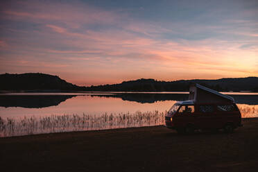 Leerer Lieferwagen am Ufer eines ruhigen Sees bei Sonnenuntergang in ruhiger Landschaft - ADSF09557