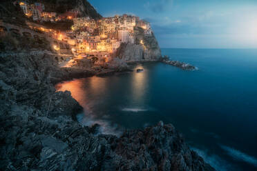 Amazing landscape with small town with colorful lights on rocky coast washing by tranquil ocean water at night - ADSF09580