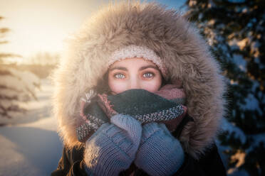 Young attractive female in warm clothing with fur joyful laughing beside covered snow conifer tree - ADSF09585