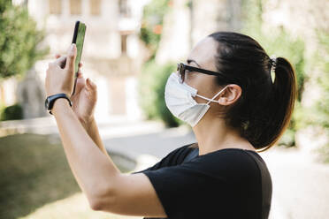 Woman wearing protective mask and taking a photo with her smartphone - XLGF00441