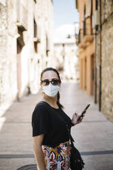 Frau trägt Schutzbrille und benutzt Smartphone in Gasse - XLGF00443