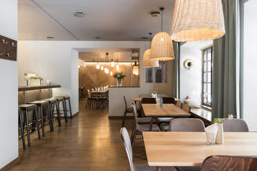 Stilvolle Lampe leuchtet über kleinen Tischen und bequemen Stühlen in einem gemütlichen Restaurant - ADSF09640