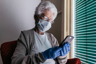 Ältere Frau beim Chatten auf dem Smartphone während der Selbstisolierung zu Hause - ADSF09695