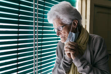 Elderly woman standing near window during pandemic - ADSF09700