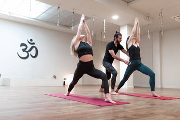 Ausgeglichene ruhige Frauen und Mann Lehrer hilft Korrektur Posen, während sie Stretching und Anhebung der Hände bis in Krieger ein Haltung auf Yoga-Klasse - ADSF09709