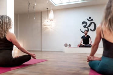 Rückenansicht von ausgeglichenen ruhigen Frauen und Mann sitzen auf Lotus-Pose mit Mudra nach auf Yoga-Klasse konzentriert - ADSF09711