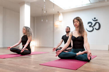 Calm Relaxer Frauen und Männer mit geschlossenen Augen sitzen auf Lotus-Pose mit Mudra Hände konzentriert nach auf Yoga-Kurs - ADSF09713
