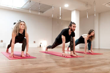 Ruhige Frauen und ein Mann, der sich beim Yoga-Kurs auf die Dehnung einer hohen Ausfallschritt-Pose konzentriert - ADSF09715