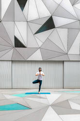Full body adult man in sportswear performing standing tree pose exercise while doing yoga against wall with geometric ornament - ADSF09731