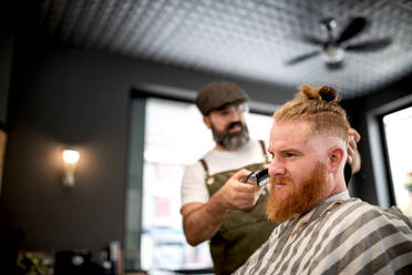 Moderne Friseur Barbier Schneiden eines erwachsenen Mannes Rothaarige Haare in Barbier Stuhl - ADSF09777