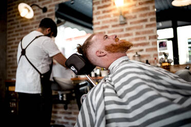 Redhead man sitting in barbershop waiting for anonymous barber on the background - ADSF09779