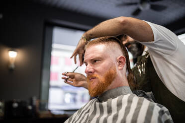 Moderne Friseur Barbier Schneiden eines erwachsenen Mannes Rothaarige Haare in Barbier Stuhl - ADSF09784