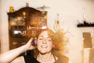 Close-up of cheerful woman listening music through headphones while dancing at home - JATF01211
