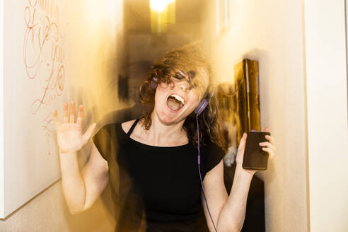 Blurred motion of woman with headphones dancing by walls at home - JATF01214