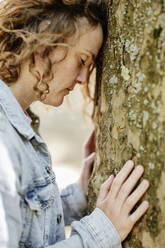 Nahaufnahme einer traurigen Frau mit geschlossenen Augen, die sich im Park an einen Baumstamm lehnt - JATF01229
