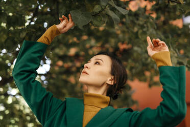 Close-up of young woman looking at leaves growing on tree - TCEF00969