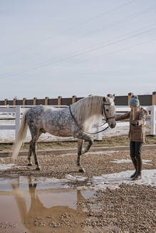 Warm gekleidete Frau mit grauem Pferd im Freien - ADSF09824
