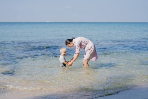 Woman and small kid having fun with water while relaxing on seacoast at resort - ADSF09835