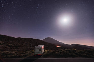 Wohnwagen am Straßenrand einer abgelegenen Wüste unter einem atemberaubenden glühenden Mond und Sternenhimmel geparkt - ADSF09873