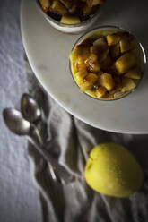Von oben Becher mit leckerem Dessert mit Apfelstückchen auf einem Teller gegen ein Tuch gelegt - ADSF09955