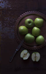 Metallmesser neben Teller mit frischen grünen Äpfeln auf schäbiger Tischplatte - ADSF09965