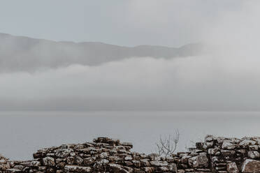 Steinmauer einer alten Burgruine gegen bewölkten Himmel mit Blick auf einen nebligen Berg - ADSF09995