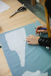 Erwachsene Frau, die ein Maßband benutzt, um ein Kleidungsstück auf dem Tisch zu messen, während sie in einer professionellen Schneiderei arbeitet - ADSF10024
