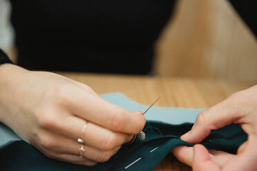 Nahaufnahme unkenntlich Schneiderin mit Nadel und Faden zu nähen benutzerdefinierte Kleidung über Tisch in professionellen Werkstatt - ADSF10027