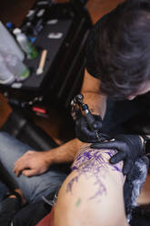 Master doing tattoo on forearm of male customer - ADSF10034