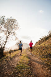 Starke aktive Männer in Sportkleidung laufen zusammen auf unbefestigten Wegen in den Bergen an einem sonnigen Herbsttag - ADSF10065