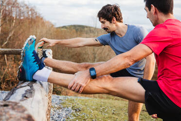 Side view of tired male joggers in blue and red shirts stretching