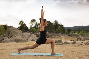 Junge Frau macht Yoga-Posen im Freien an einem bewölkten Tag neben einem Damm Strand - ADSF10094