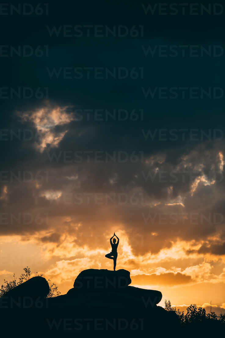 Silhouette of woman doing yoga poses outdoors on a amazing sunset while  standing on rock stock photo