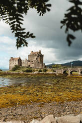 Amazing scenery of abandoned medieval castle with cobblestone bridge across colorful spotted swampy shore under dramatic cloudy sky in Scotland - ADSF10114