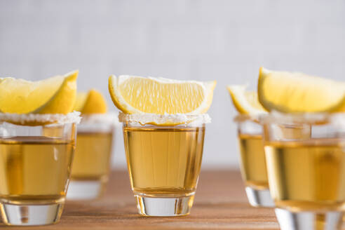 Reihe von Glas Töpfe mit goldenen Tequila und Zitronenscheiben auf Holztisch mit weißer Wand auf unscharfen Hintergrund - ADSF10147