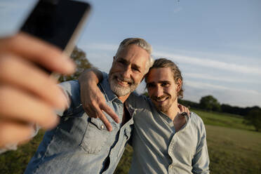 Glücklicher Vater mit erwachsenem Sohn macht ein Selfie auf einer Wiese auf dem Lande - KNSF08305