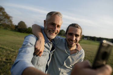 Happy father with adult son taking a selfie on a meadow in the countryside - KNSF08306
