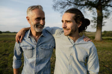 Happy father and adult son embracing on a meadow in the countryside - KNSF08308