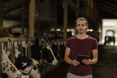 Porträt eines jungen Landwirts mit Tablet im Kuhstall auf einem Bauernhof - KNSF08327