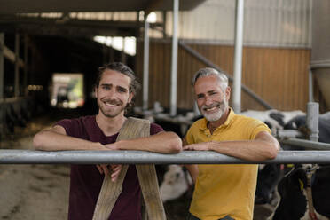 Porträt eines lächelnden reifen Landwirts mit erwachsenem Sohn im Kuhstall auf einem Bauernhof - KNSF08339