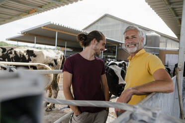 Lächelnder reifer Bauer mit erwachsenem Sohn im Kuhstall auf einem Bauernhof - KNSF08345