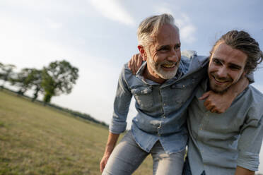 Glücklicher Vater und erwachsener Sohn spielen auf einer Wiese auf dem Lande miteinander - KNSF08398