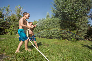 Kleine Kinder in Badekleidung spritzen Wasser und halten einen Gartenschlauch zusammen - ADSF10156