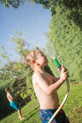 Kleiner Junge in Badekleidung, der sich mit Wasser aus dem Gartenschlauch bespritzt - ADSF10159