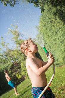 Kleiner Junge in Badekleidung, der sich mit Wasser aus dem Gartenschlauch bespritzt - ADSF10159