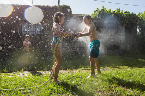 Kleine Kinder in Badekleidung, die herumrennen und sich gegenseitig mit Wasser aus dem Gartenschlauch bespritzen - ADSF10160