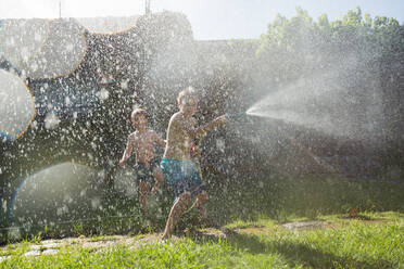 Kleine Kinder in Badekleidung, die herumrennen und sich gegenseitig mit Wasser aus dem Gartenschlauch bespritzen - ADSF10161