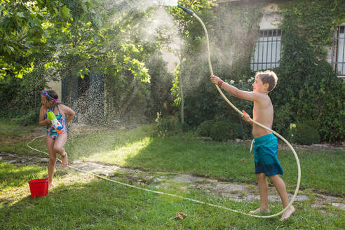Kleine Kinder in Badekleidung, die herumrennen und sich gegenseitig mit Wasser aus dem Gartenschlauch bespritzen - ADSF10164